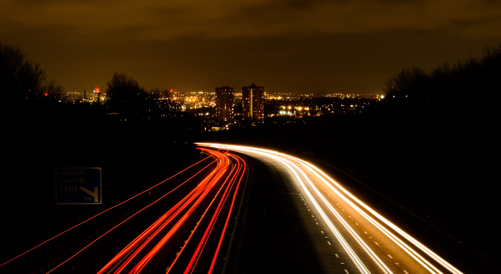 A motorway at night: red and white light trails running towards the city